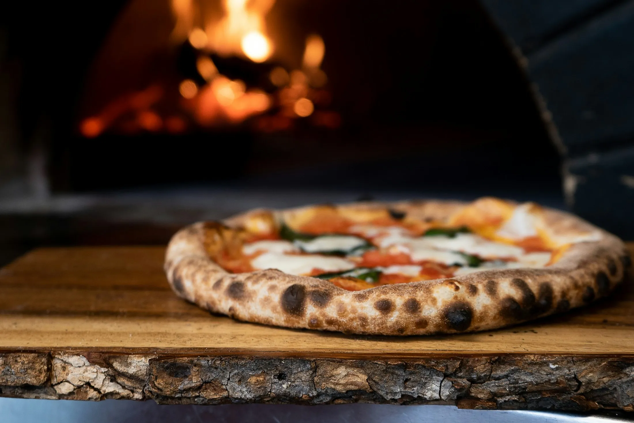Une pizza qui sort du four, posée devant le feu